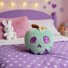 Plush toy apple with purple spots on a bed with polka dot bedding and heart decorations.
