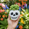White skull-shaped object with green succulent held in a hand against a colorful floral background