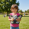 Child holding a colorful butterfly-shaped toy with a skull design in a park.