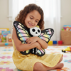 Child holding a butterfly-shaped plush toy with a skull design in a room with toys in the background.