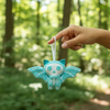 Blue bat-shaped keychain held by a hand against a forest background