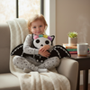 Child sitting on a couch holding a plush toy with a rainbow bow, surrounded by a cozy living room setting.