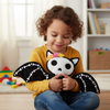 Child holding a black and white plush toy with colorful accents in a room with toys and books.