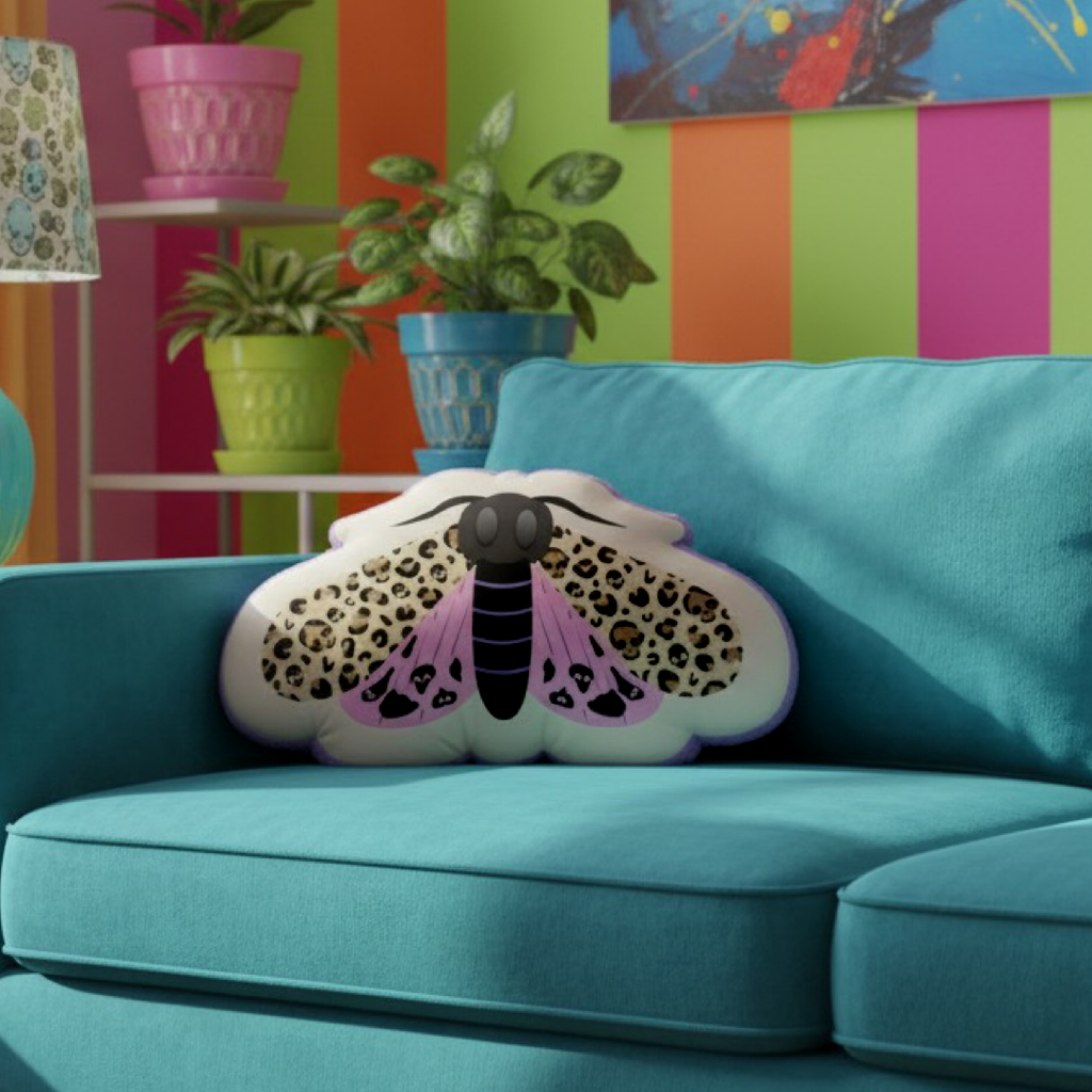 Decorative pillow shaped like a moth on a teal couch with colorful wall and plants in the background