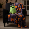 Green ghost plush toy on a chair with a Halloween-themed blanket
