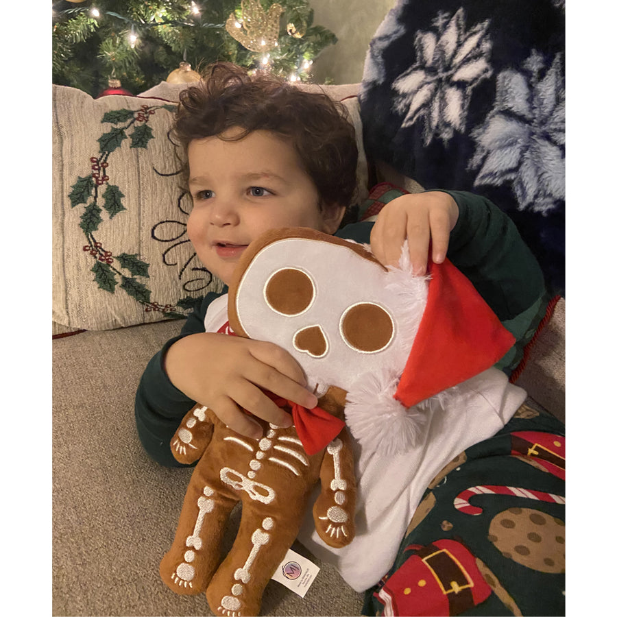 child holding a 12 inch tall gingerdead skeleton plush in a red santa hat with a red bow tie made in brownminky white embroidery beautiful embroidery high quality plush halloween skeleton bat plushie halloween goth home decor childrens halloween christmas or creepmas skeleton plush toy