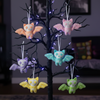 Colorful bat-shaped ornaments hanging from a decorated tree with purple lights.